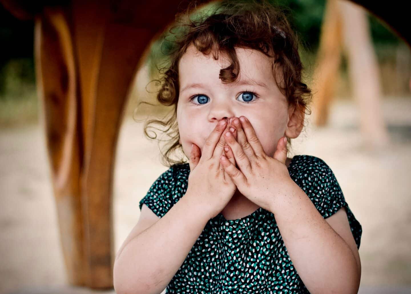 little girl with hand over mouth